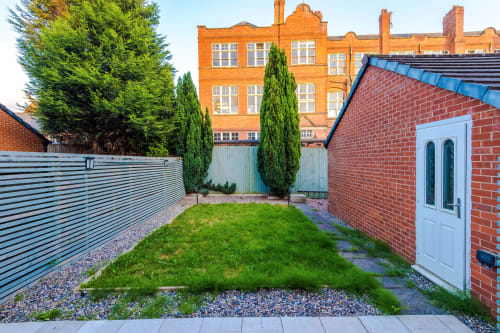 Vidale Court villa garden in Manchester with green lawn, brick walls, white door, and modern fencing