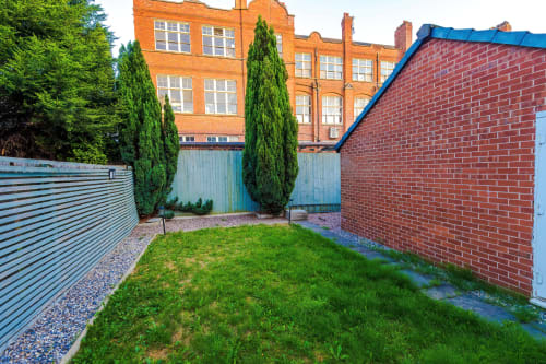 Private garden courtyard at Vidale Court Manchester villa with green lawn, brick walls, and mature cypress trees
