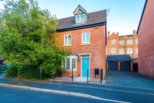 Modern brick villa at Vidale Court in Manchester with blue door, driveway, and garden greenery
