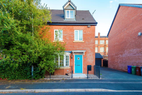 Vidale Court villa in Manchester - 4-bedroom brick home with turquoise door, dormer window, and lush garden hedging