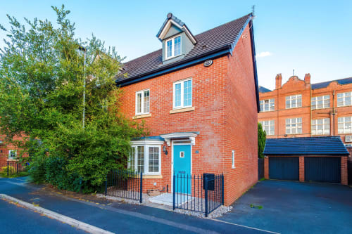 Modern red brick villa in Manchester with blue door, driveway, and mature landscaping at Vidale Court