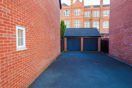 Private driveway with blue garage doors at Vidale Court villa in Manchester, showing red brick walls and free parking