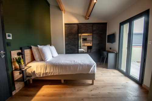 Modern studio apartment at Lieu-dit Boulage with bed, green accent wall, wooden floors, and terrace access