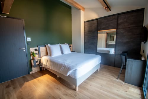 Modern studio apartment bedroom at Lieu-dit Boulage with green accent wall, white bed, dark wardrobe, and wooden flooring in