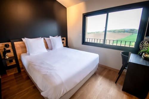 Modern bedroom at Lieu-dit Boulage hotel with white bed, countryside view, dark accent wall, and wooden floor.