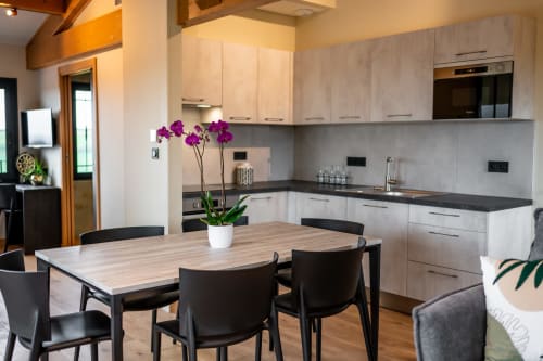 Modern kitchen and dining area in Lieu-dit Boulage Premium apartment with white cabinetry, black chairs, and purple orchids