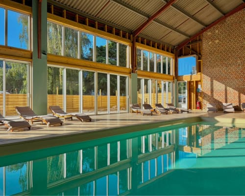 Piscine intérieure du Domaine Les Racines avec transats et grandes fenêtres sur le parc