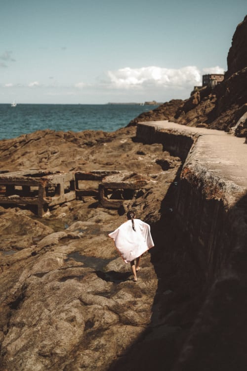 Femme en robe blanche explorant la côte rocheuse de l'Hôtel Saint Enogat à Dinard