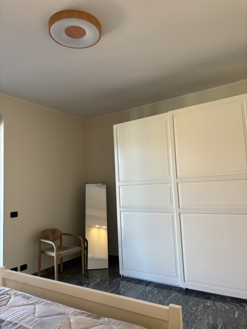 Camera da letto spaziosa nell'appartamento Casa Vacanze Luna, Seriate, con armadio bianco, specchio, sedia in legno e illuminazione moderna