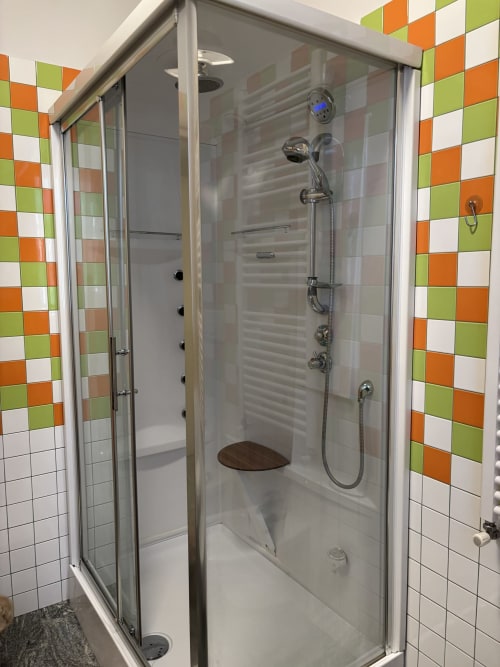 Moderno box doccia con porte in vetro, accessori cromati e piastrelle bianche con accenti colorati verde e arancione