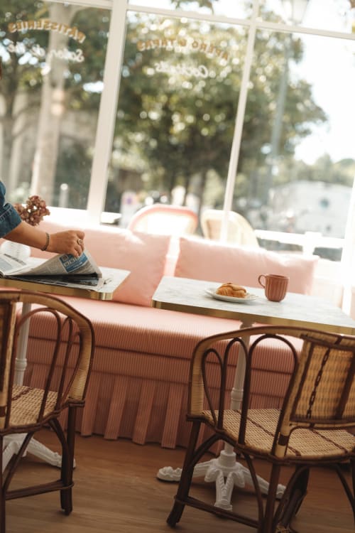 Salon de café lumineux à l'Hôtel Saint Enogat à Dinard avec banquette rose, croissant et vue sur les arbres