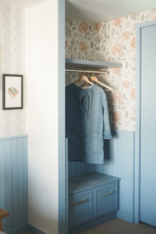Penderie d'une chambre d'hôtel à Dinard avec banc bleu, cintres en bois et papier peint floral