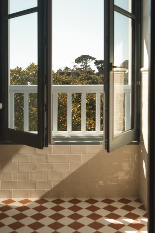 Portes noires ouvertes révélant un balcon à balustrade blanche avec vue sur un jardin luxuriant et des arbres, chambre Hôtel Saint Enogat Dinard