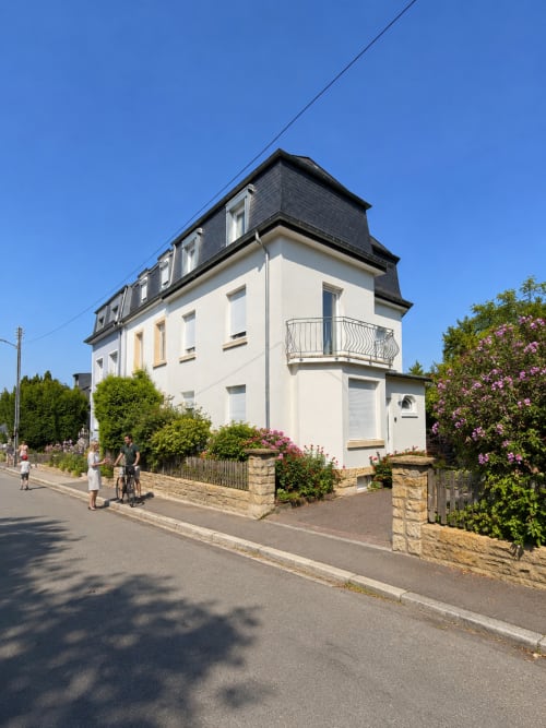 Villa Mattbnb à Metz : façade crème, toit mansardé, jardins fleuris et vue sur rue par beau temps