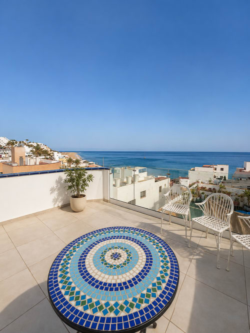 Penthouse-Terrasse in Morro Jable mit dekorativem blauem Mosaiktisch, Meerblick und weißem Mobiliar mit Mittelmeerblick