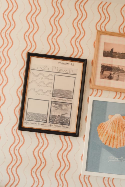 Illustrations marines vintage encadrées et photographies côtières exposées sur papier peint à motifs ondulés corail à l'Hôtel Saint Enogat,