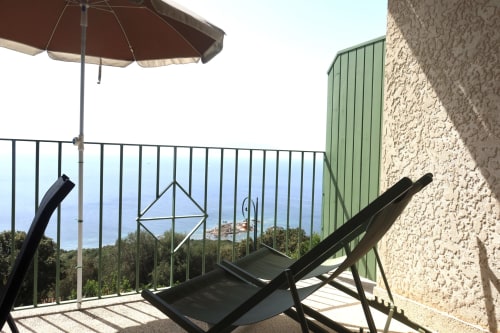 Terrasse avec vue sur mer à la Résidence Roc E Mare, parasol, transats et bâtisse en pierre à Cargèse