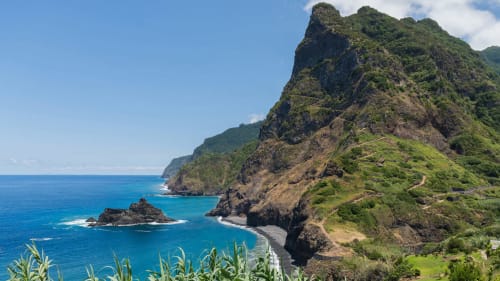 Escarpas costeiras dramaticamente erguidas com vegetação luxuriante sobre águas turquesas perto de Porto Moniz, Portugal