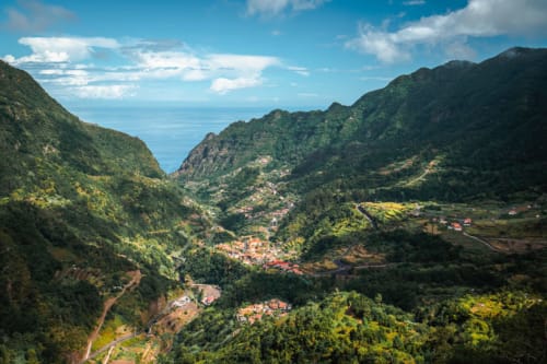 Vale exuberante com edifícios de telhados vermelhos aninhados entre montanhas verdes, avistando o Oceano Atlântico no Porto