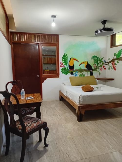 Habitación Tucán del hostal Cayuco Maya en Bacalar con cama de madera, mural de tucán, aire acondicionado y ventilador