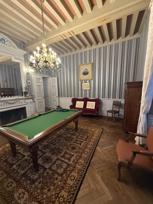 Élégante salle de billard du Château de Montbrault avec papier peint rayé, lustre, cheminée et mobilier d'époque