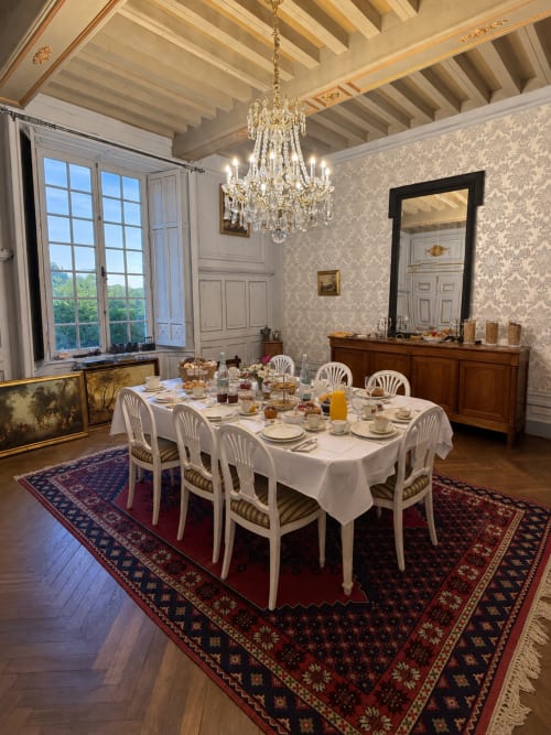 Salle à manger élégante du Château De Montbrault avec lustre, chaises blanches et table dressée formellement à Fleurigné, France