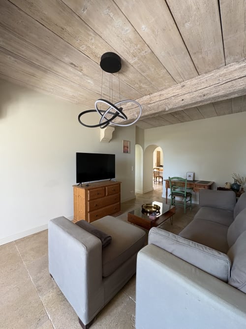Salon moderne à la Conciergerie Maurin, Arles avec fauteuils gris, meuble TV en bois, poutres apparentes et style contemporain
