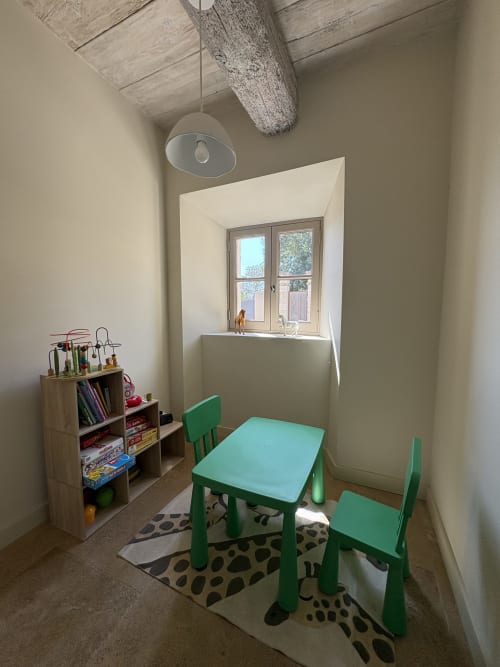 Chambre d'enfant avec table et chaises vertes, étagère en bois avec jouets et livres, lumière naturelle de la fenêtre, Mas en Camargue