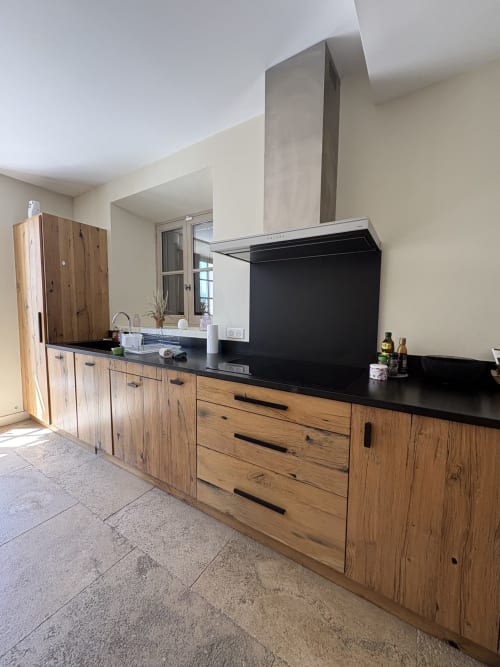 Cuisine contemporaine avec meubles en bois, plan de travail noir et hotte en inox à la Conciergerie Maurin à Arles