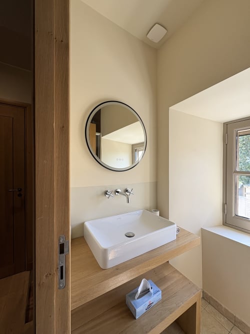 Salle de bains moderne avec vasque blanche, miroir noir rond et meuble en bois à la Conciergerie Maurin à Arles