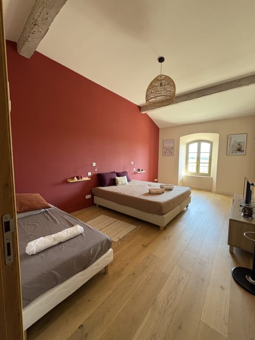 Spacieuse chambre à la Conciergerie Maurin à Arles avec mur d'accent rouge, deux lits, parquet et fenêtre cintrée