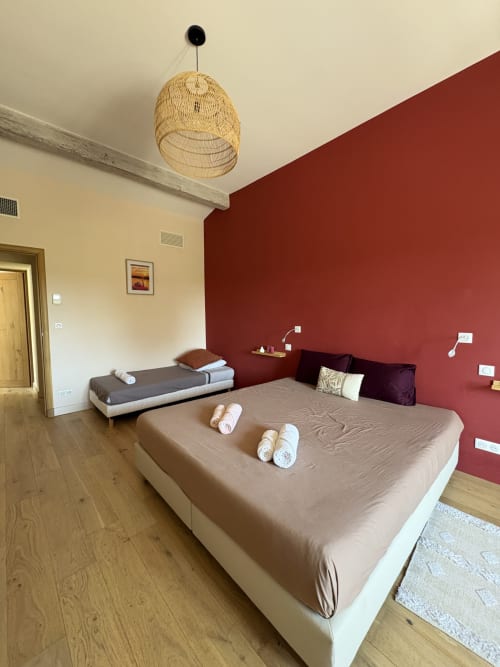 Chambre moderne à la Conciergerie Maurin à Arles avec lit queen-size, lit simple, suspension en osier et mur d'accent bordeaux