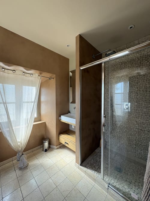 Salle de bains moderne à la Conciergerie Maurin à Arles avec douche à l'italienne carrelée, lavabo sur colonne et fenêtre.