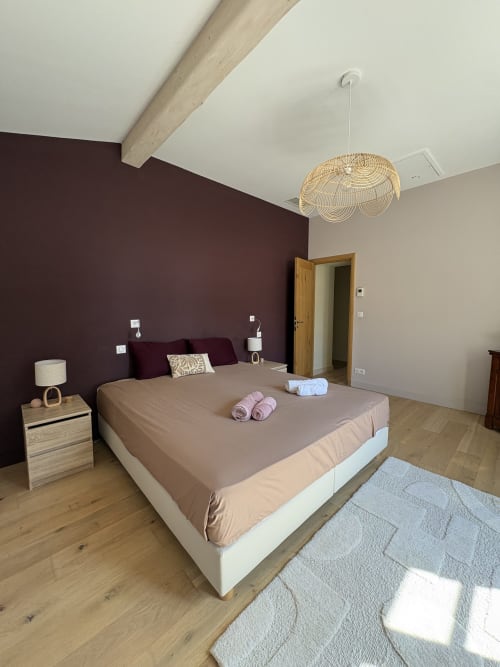 Chambre moderne à la Conciergerie Maurin à Arles avec mur d'accent bordeaux profond, lit beige, luminaire suspendu tressé et bois