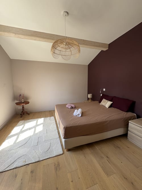 Chambre moderne à la Conciergerie Maurin à Arles avec lit queen-size, mur d'accent bordeaux, luminaire suspendu tressé et poutres en bois