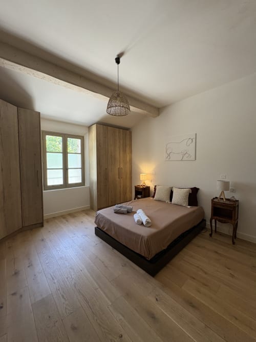 Chambre spacieuse à la Conciergerie Maurin à Arles avec armoire en bois, lit queen-size, bureau, luminaire suspendu et parquet.