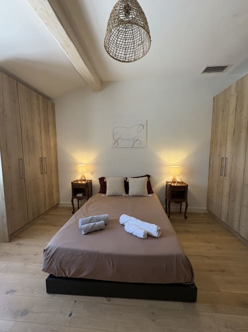 Chambre spacieuse à la Conciergerie Maurin à Arles avec lit, serviettes roulées, armoires en bois, lampes de chevet et suspension tissée