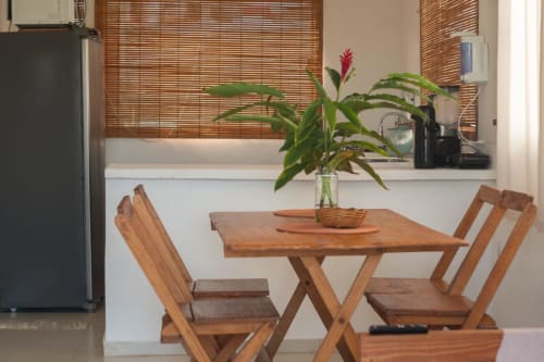 Mesa de jantar em madeira com cadeiras e flores frescas no apartamento Vila Pitangueira em Uruçuca, Brasil