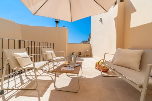 Terraza soleada de Casa Abeurador en Artà con tumbonas, sombrilla y vistas a la ciudad desde esta encantadora casa antigua