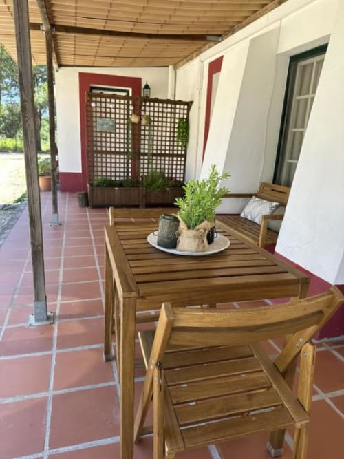 Pátio coberto com mesa de madeira e cadeiras para refeições na pousada Monte da Tojeirinha em Montargil, Portugal