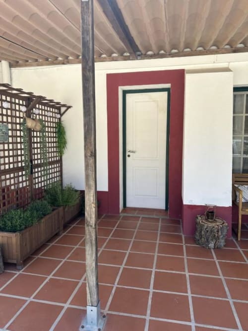 Pátio coberto com azulejos em tons de terracota, porta branca com moldura vinho em Monte da Tojeirinha, Montargil