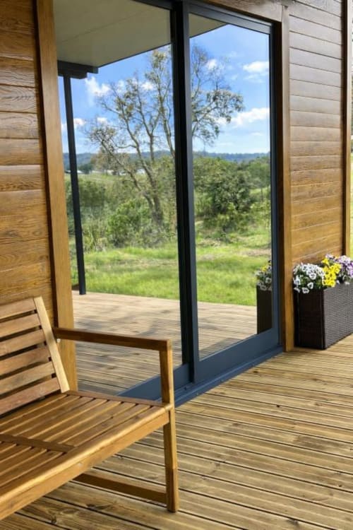 Terraço de madeira com cadeira vista para vale verde e montanhas, varanda do bungalow Monte da Tojeirinha com vista para lago
