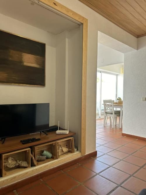 Sala de estar moderna com móvel de TV em madeira, televisão de tela plana e passagem aberta para a área de jantar na villa Monte da Tojeirinha