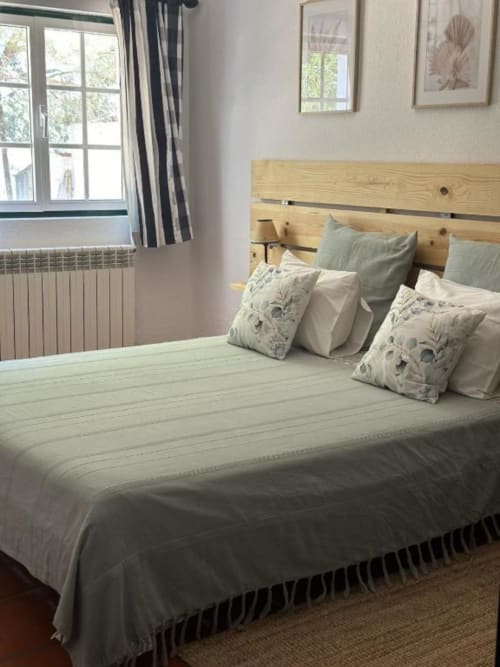 Quarto luminoso com cabeceira de madeira natural, roupa de cama em camadas e almofadas decorativas na quinta Monte da Tojeirinha, Montargil