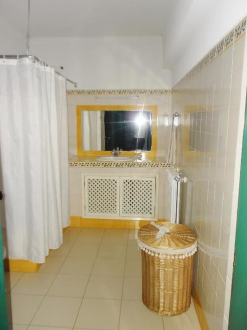 Banheiro luminoso com espelho de moldura amarela, paredes de azulejo bege, criado com portas de treliça e cesto de vime para roupa