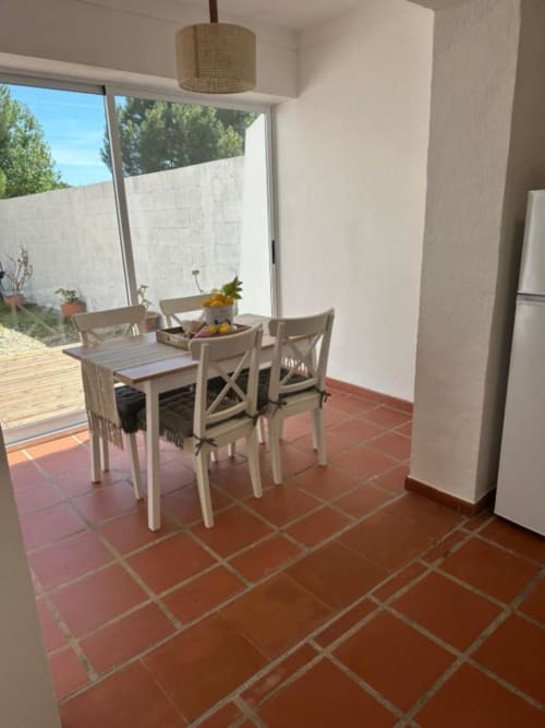 Zona de refeições com mesa e cadeiras brancas sobre azulejos de terracota, abrindo para o pátio da villa Monte da Tojeiranha em Montargil