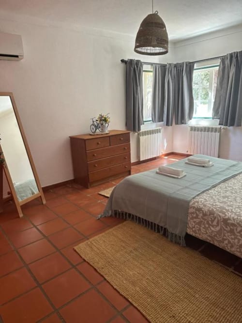 Quarto espaçoso da villa Monte da Tojeirinha em Montargil com pisos em terracota, cômoda de madeira, cortinas cinzentas e tecidos naturais