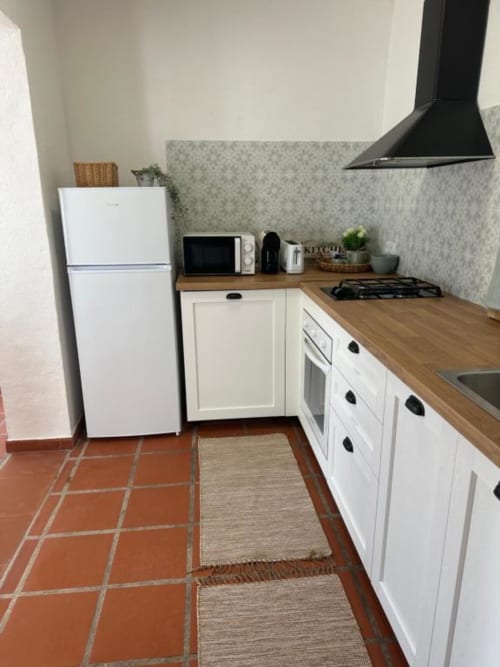 Cozinha moderna na villa Monte da Tojeirinha com armários brancos, bancada em madeira, fogão, micro-ondas e geladeira branca