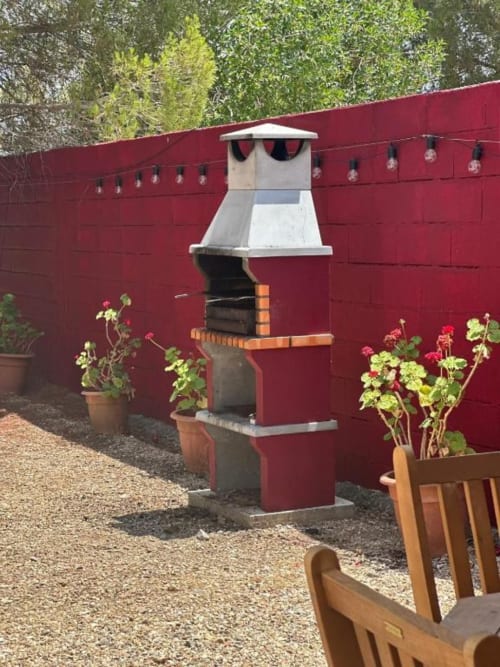 Churrasqueira ao ar livre no pátio da villa Monte da Tojeirinha com cerca vermelha e vasos de flores em flor