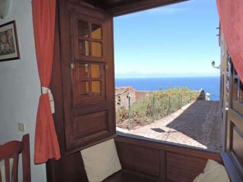 Vista del estudio desde puertas de madera abiertas con vistas a viñedos y mar azul en Casa Rural Los Helechos, Agulo